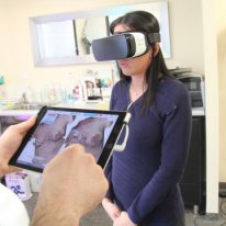 une personne tient une tablette devant une femme portant un casque de réalité virtuelle